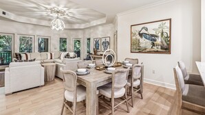 A spacious living room with a dining area, large windows, and a ceiling light fixture. - Picturesque Villa w/ Screened Porch & Amenities (Hilton Head Island)