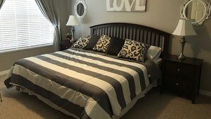 A bedroom with a large bed, two nightstands, a bedside lamp, a mirror, a window with curtains, and a 'LOVE' sign on the wall. - 4 bedroom townhouse at The Villas at seven Dwarfs (Kissimmee)