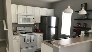 A modern kitchen with white cabinets, a stainless steel refrigerator, a microwave, and a coffee maker. - 4 bedroom townhouse at The Villas at seven Dwarfs (Kissimmee)