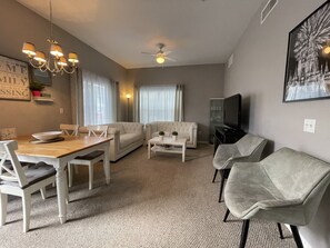 A living room with a dining table, two sofas, a coffee table, a TV, and a ceiling fan.