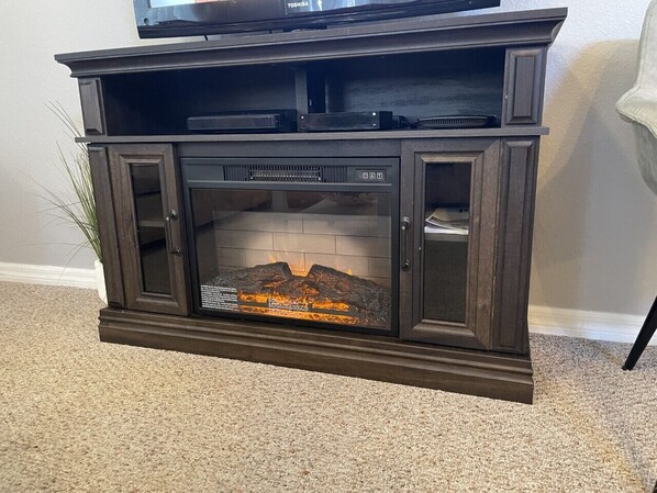 A dark wooden entertainment center with a built-in fireplace, a flat-screen TV on top, and a plant beside it.