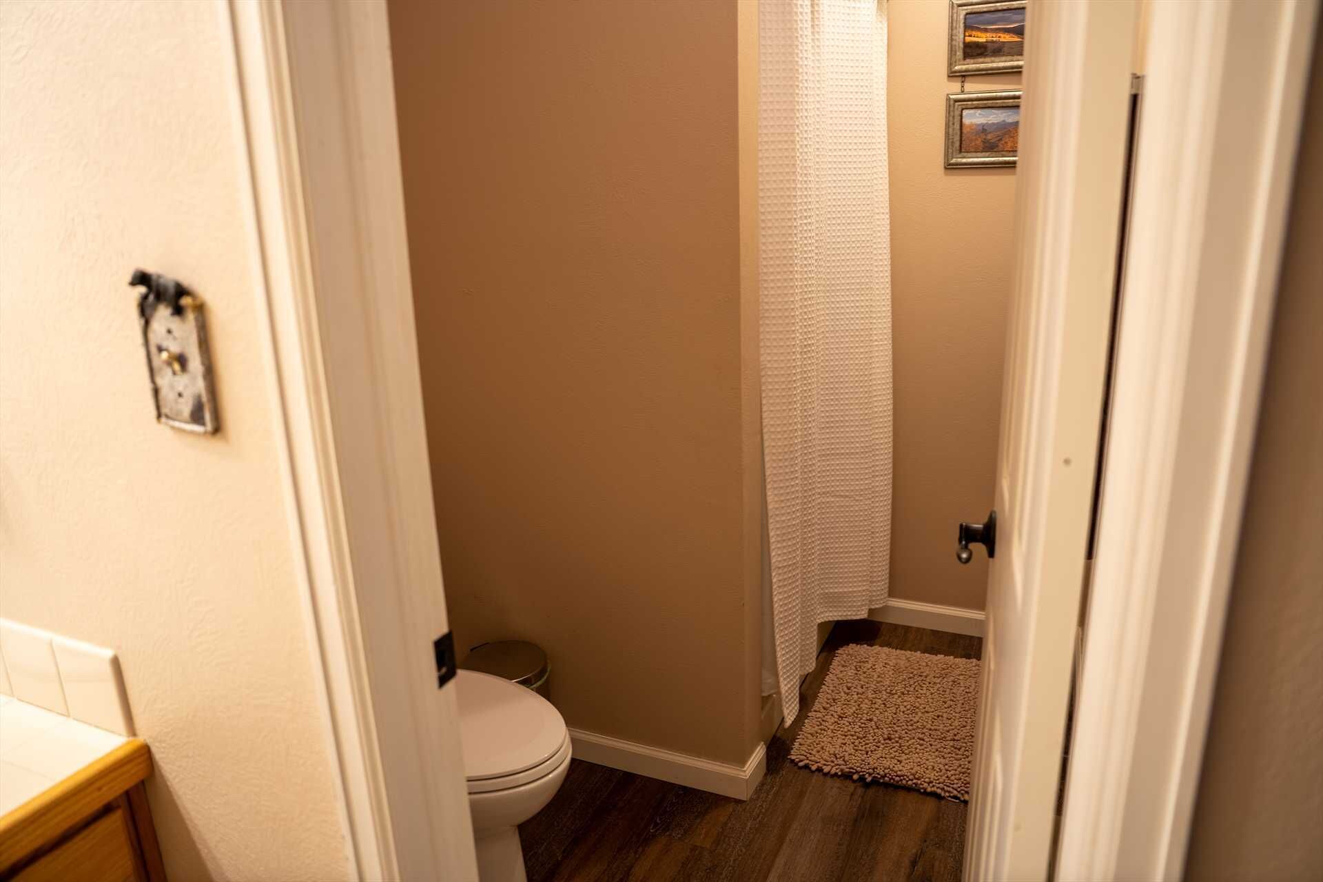 Ein schmaler Flur führt zu einem Badezimmer mit Toilette, Duschvorhang und einem kleinen Teppich.