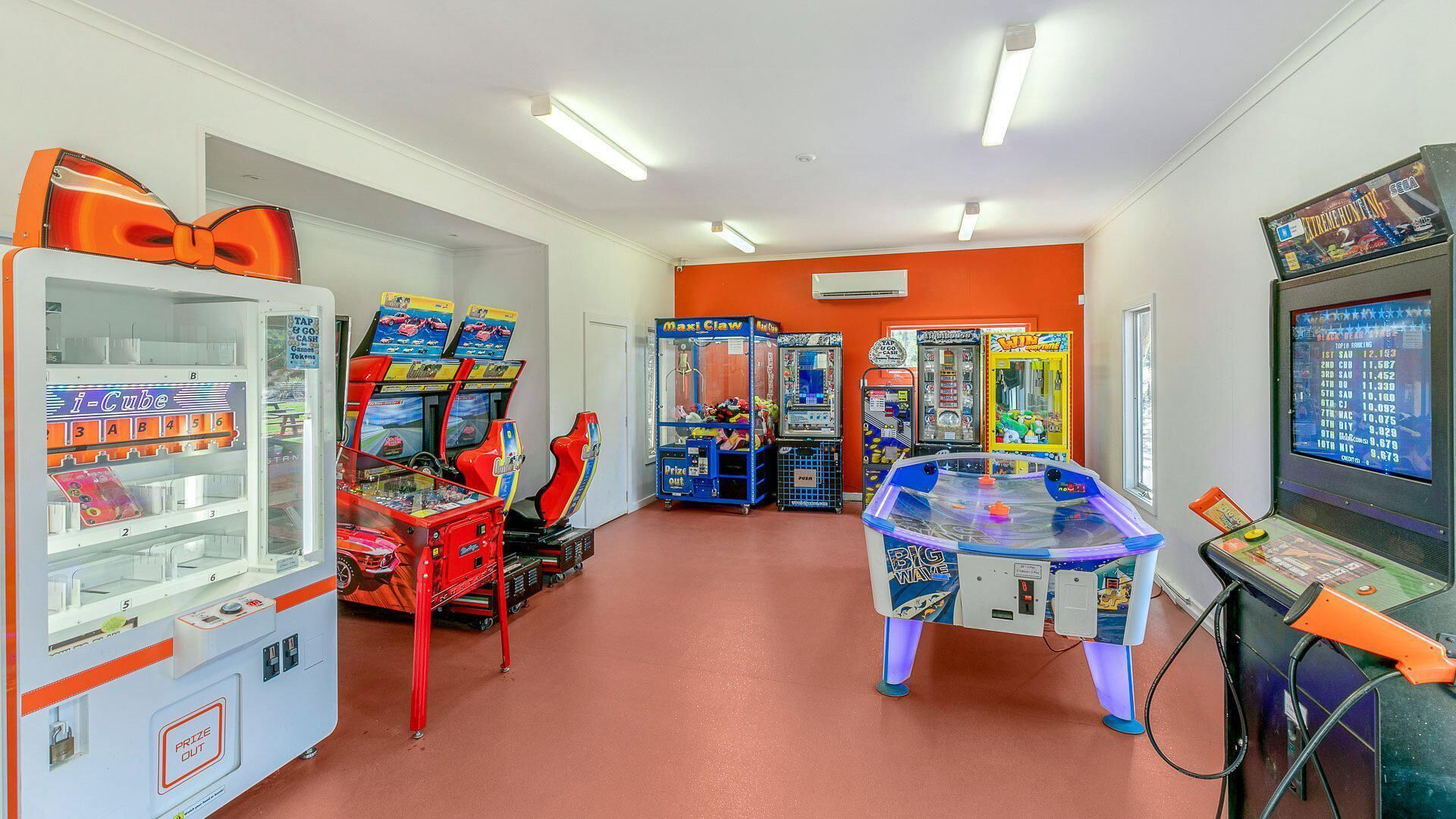 A row of arcade machines and claw games in a brightly lit room with orange walls and a red floor.