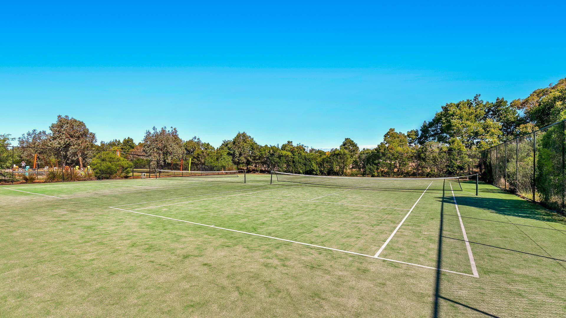 Een tennisbaan met een net, omgeven door bomen en een heldere lucht.