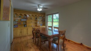A dining area with a wooden table and chairs, a ceiling fan, and a bookshelf filled with books and decorative items. - Close to a Vibrant and fun DownTown Rose District. 15 min from Tulsa. (Broken Arrow)