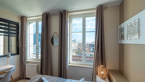 A bedroom with a bed, a desk, a chair, a radiator, a window with curtains, and a wall-mounted lamp. - Les Mouailleries on the ground floor 2 bedrooms 2 bathrooms (Honfleur)
