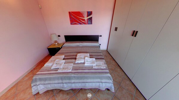 Habitación de hotel con cama, mesita de noche, lámpara, un cuadro en la pared y armario.