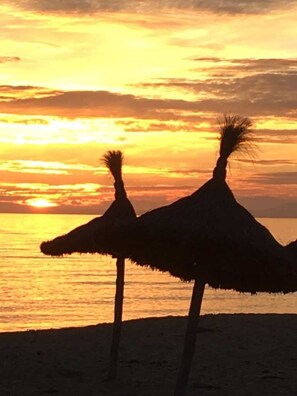 Deux parasols de paille sur une plage au coucher du soleil.