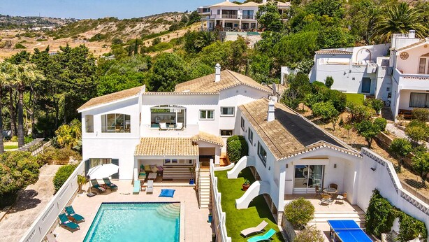Eine moderne Villa mit Swimmingpool, Sitzgelegenheiten im Freien und Blick auf die umliegende Landschaft.