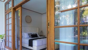 A bedroom with a bed, a bedside table, a round wall decoration, and a view of a pool through a glass door. - Interconnection Hostel (Kuta)