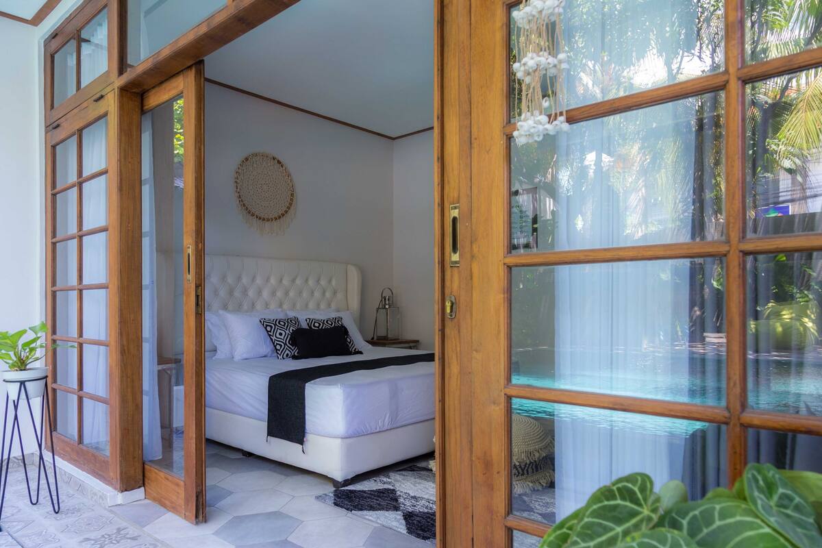 A bedroom with a bed, a bedside table, a round wall decoration, and a view of a pool through a glass door.
