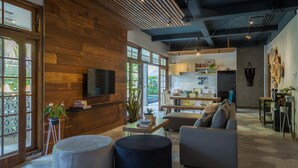 A modern living room with a wooden wall, a flat-screen TV, and a dining area with a kitchen in the background. - Interconnection Hostel (Kuta)
