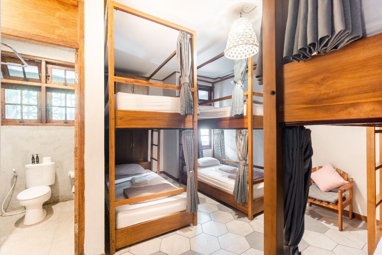 Una habitación con literas, un armario de madera, un inodoro y una ventana con cortinas.