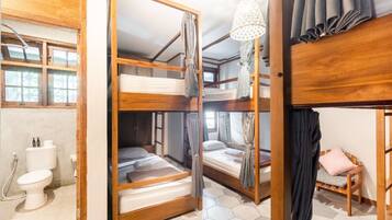 Una habitación con literas, un armario de madera, un inodoro y una ventana con cortinas.