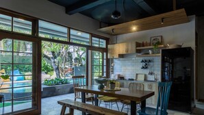 A modern kitchen with large windows, wooden furniture, and a view of a garden. - Interconnection Hostel (Kuta)