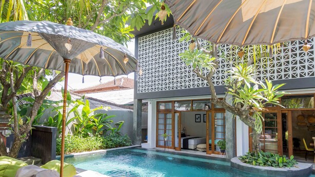 A pool area with lounge chairs, a pergola, and a building with a lattice facade. - Interconnection Hostel (Kuta)