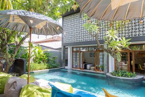 A pool area with lounge chairs, a pergola, and a building with a lattice facade.