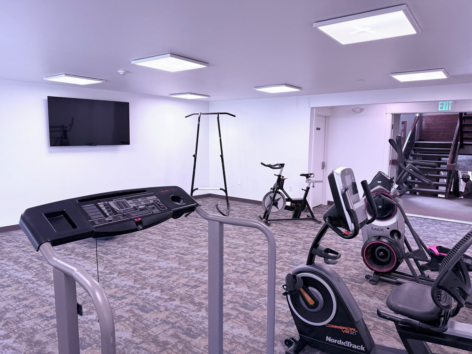 A gym with cardio machines, a stationary bike, and a TV mounted on the wall.