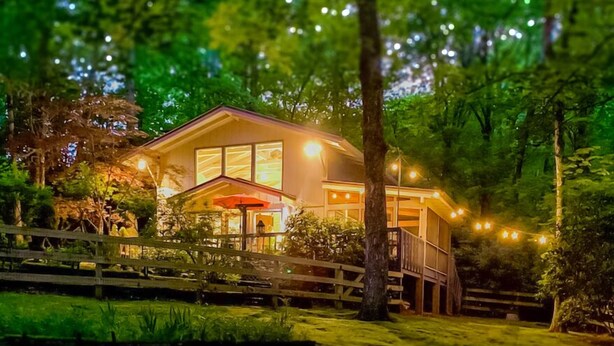 Uma casa com varanda e luzes de Natal, cercada por árvores.