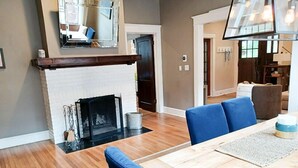 A dining area with a wooden table and blue upholstered chairs, a fireplace with a white mantel, and a large mirror on the wall. - Classic VAHi Bungalow (Atlanta)