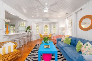 A bright, white interior with a blue coffee table, a blue sofa, and a wicker chair. - Southern Luxury with Private Pool + Hot Tub, Near Beach by Tybee Cottages (Tybee Island)