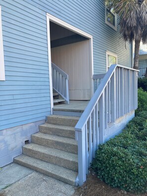 A house with a front porch, a set of concrete steps leading to the entrance, and a small garden area with greenery. - Villas on the Gulf.  Pool view and Only 3 Min Walk To The Beach (Pensacola Beach)