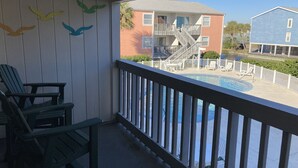 Un balcón con piscina, sillas de madera y vista a un edificio con escaleras.