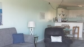 Un salon avec un canapé gris, une table basse en verre et un coin repas comprenant une table et des chaises.