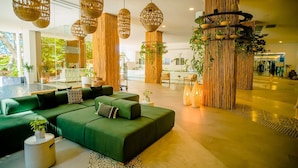 A modern lobby with a green sofa, hanging wicker lamps, and vertical bamboo panels.