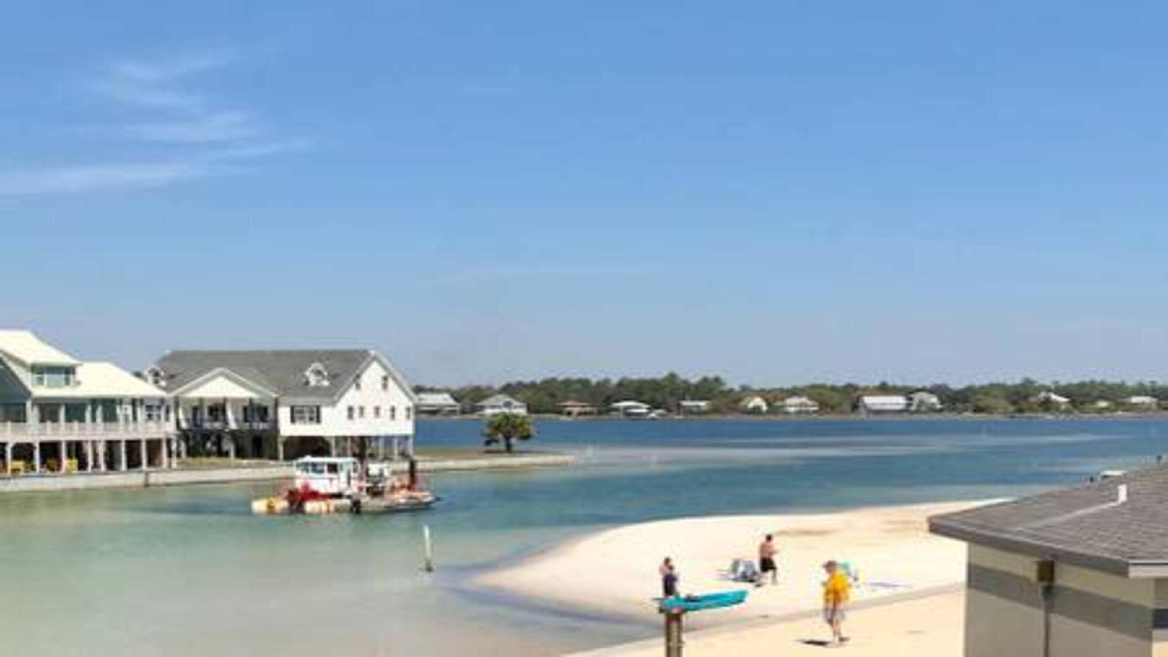 A coastal view with a sandy beach, a boat, and buildings in the background.