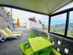Eine Terrasse mit gelben Lounge-Stühlen, einem grünen Tisch und Blick auf die Landschaft.