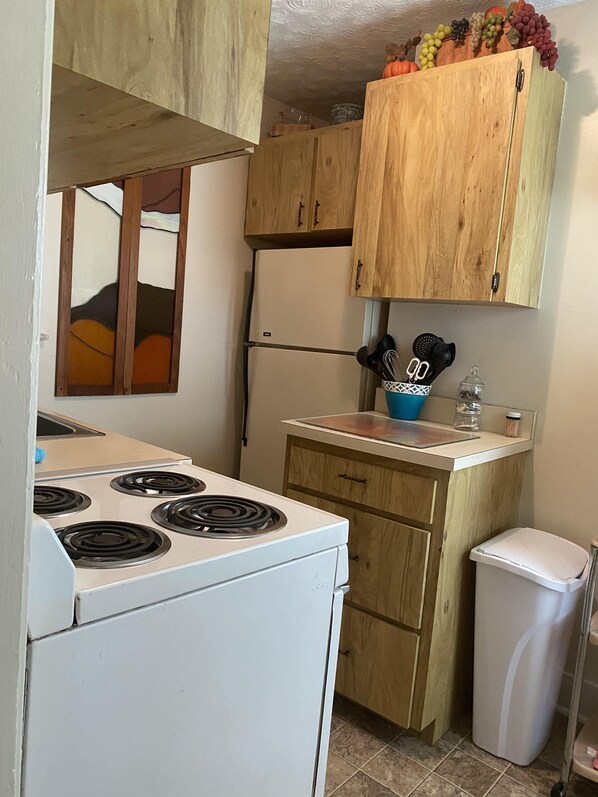 Een praktische keuken met een wit fornuis, houten kastjes, een klein aanrecht en een vuilnisbak.