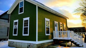 A green house with a white porch and steps leading up to it.