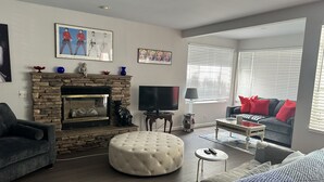 A living room with a stone fireplace, a flat-screen TV, a grey sofa with red cushions, and a grey armchair. - Downtown-PALM-SPRINGS-Get-AWAY (Palm Springs)