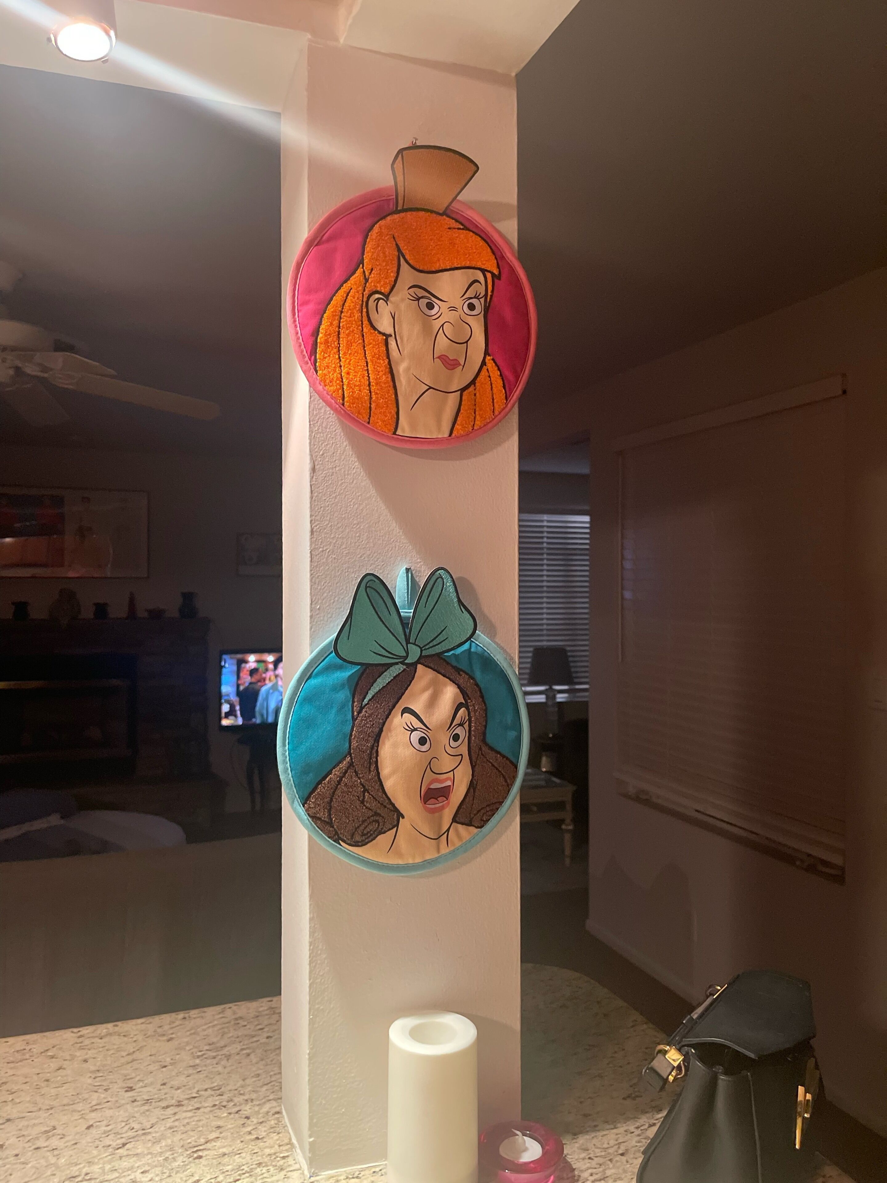 A wall with two circular wall hangings, a white candle, and a black bag on the floor.