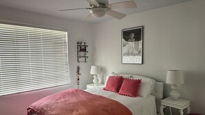 A bedroom with a bed, two bedside tables with lamps, a ceiling fan, a window with blinds, and wall art. - Downtown-PALM-SPRINGS-Get-AWAY (Palm Springs)
