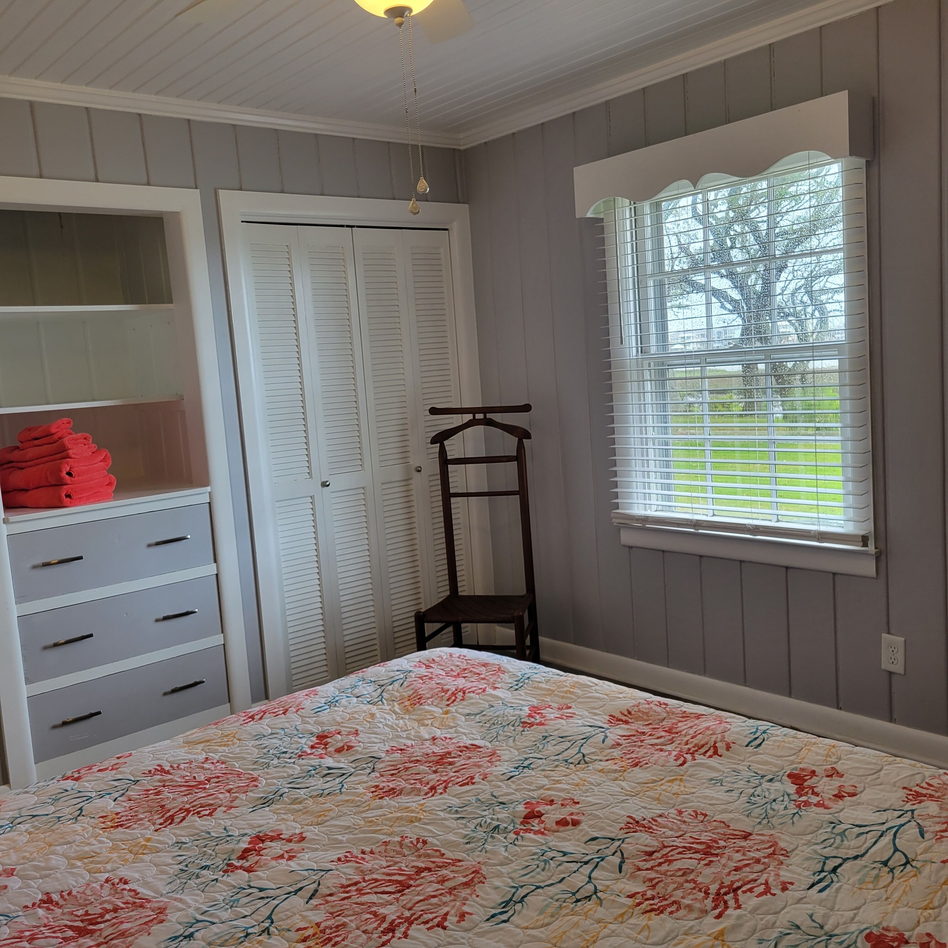 A bedroom with a bed, a wardrobe, a chair, and a window with blinds.