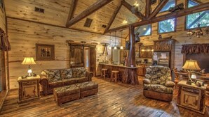 A rustic cabin interior with wooden floors, a large sofa, a dining area, and a bar.