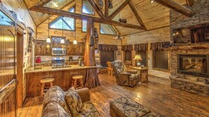 A log cabin interior with a stone fireplace, wooden floors, and a cozy seating area.
