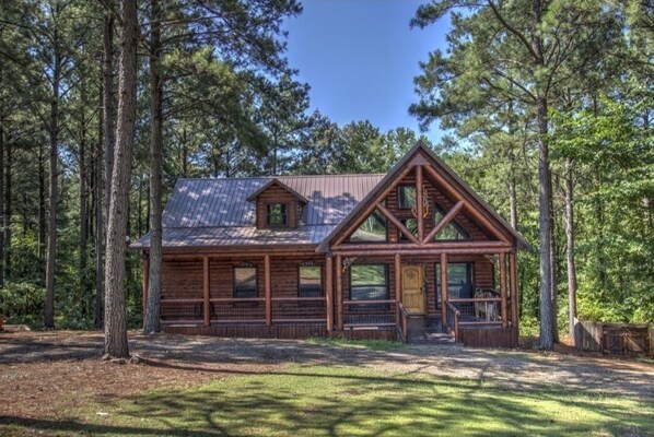 A log cabin with a gabled roof, a front porch, and a large window. - Timber Bear Cabin - Your Perfect Getaway, Firepit/Jacuzzi/WiFi/Much More! (Broken Bow)