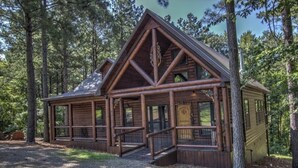 A log cabin with a porch, surrounded by trees.
