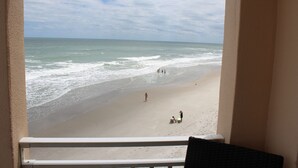 Uitzicht op een strand vanaf een balkon met een hekwerk, een zandstrand en de oceaan.