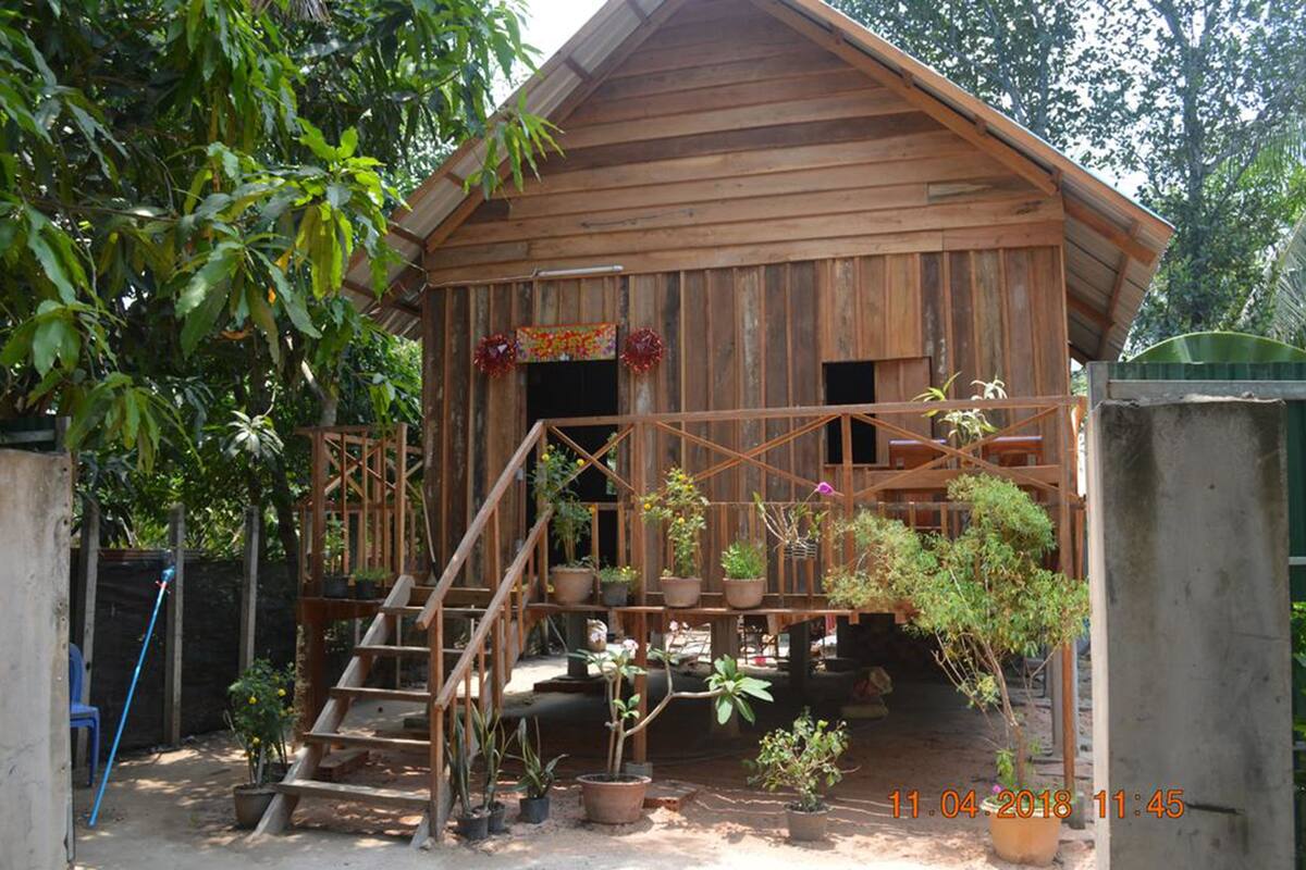 A wooden building with a porch, surrounded by potted plants and a staircase leading up to it.