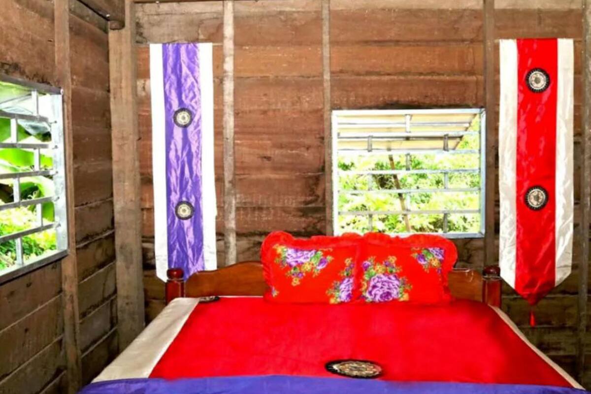 A wooden room with a bed, curtains, and a window.