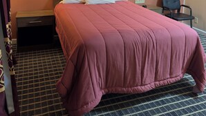 A hotel room with a large bed, two bedside lamps, a nightstand, a chair, and a painting on the wall. - Boone Trail Inn (Middlesboro)