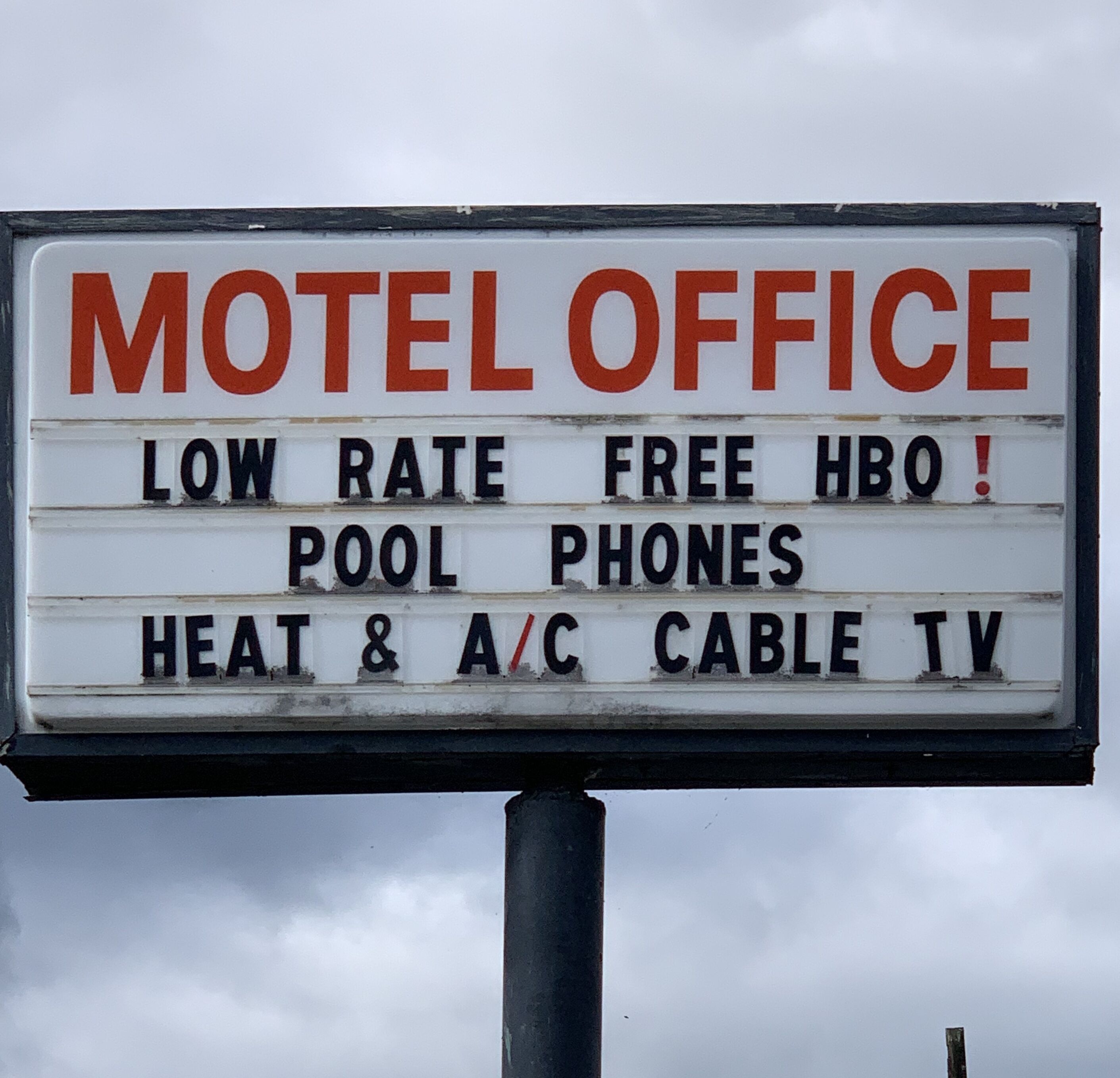 A motel office sign listing amenities such as low rate, free HBO, pool, phones, heat, A/C, and cable TV.