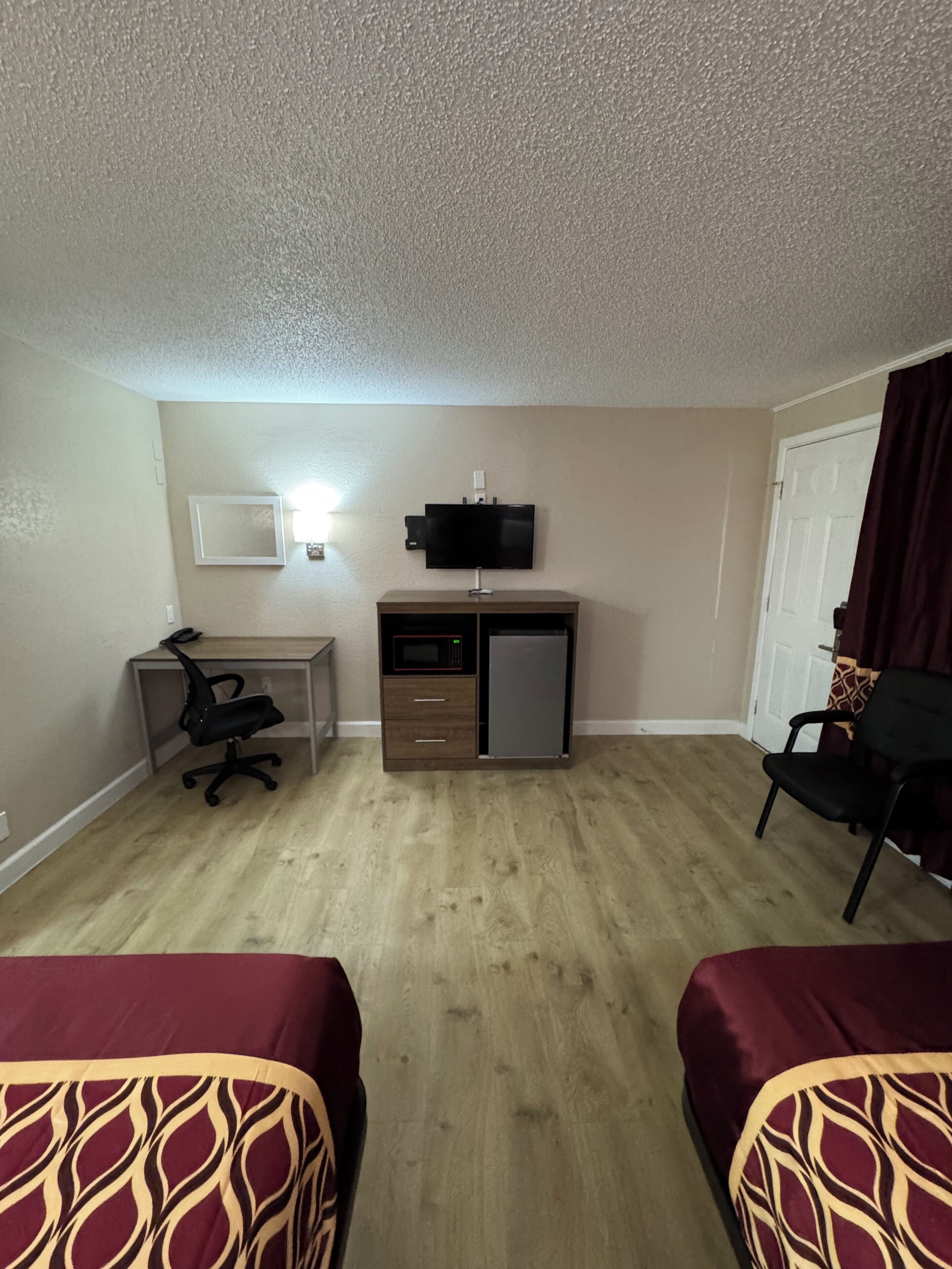 Una habitación de hotel con dos camas, un escritorio con silla, televisor, microondas y refrigerador.