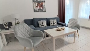 A modern living room with a sofa, two armchairs, a coffee table, and a side table with a lamp. - SÜ 1; 2-space; mezzanine; 2 balconies; 58m² - house south beach (Sierksdorf)