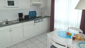 A kitchen with white cabinets, a stove, a sink, and a dining table with a blue placemat. - SÜ 1; 2-space; mezzanine; 2 balconies; 58m² - house south beach (Sierksdorf)