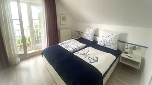 A bedroom with a bed, a nightstand, a window with curtains, and a radiator. - SÜ 1; 2-space; mezzanine; 2 balconies; 58m² - house south beach (Sierksdorf)